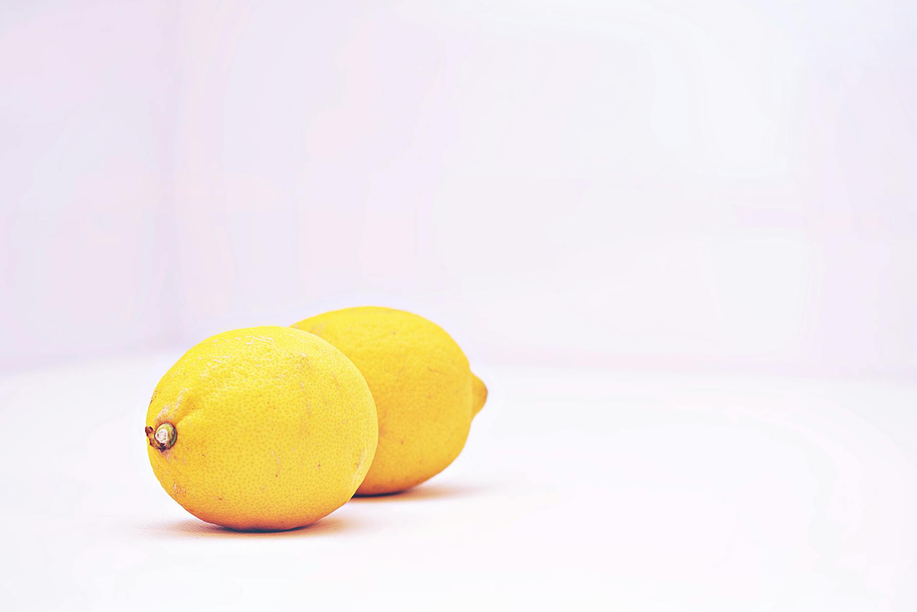 Two vibrant lemons placed against a minimalistic white background, showcasing freshness and simplicity