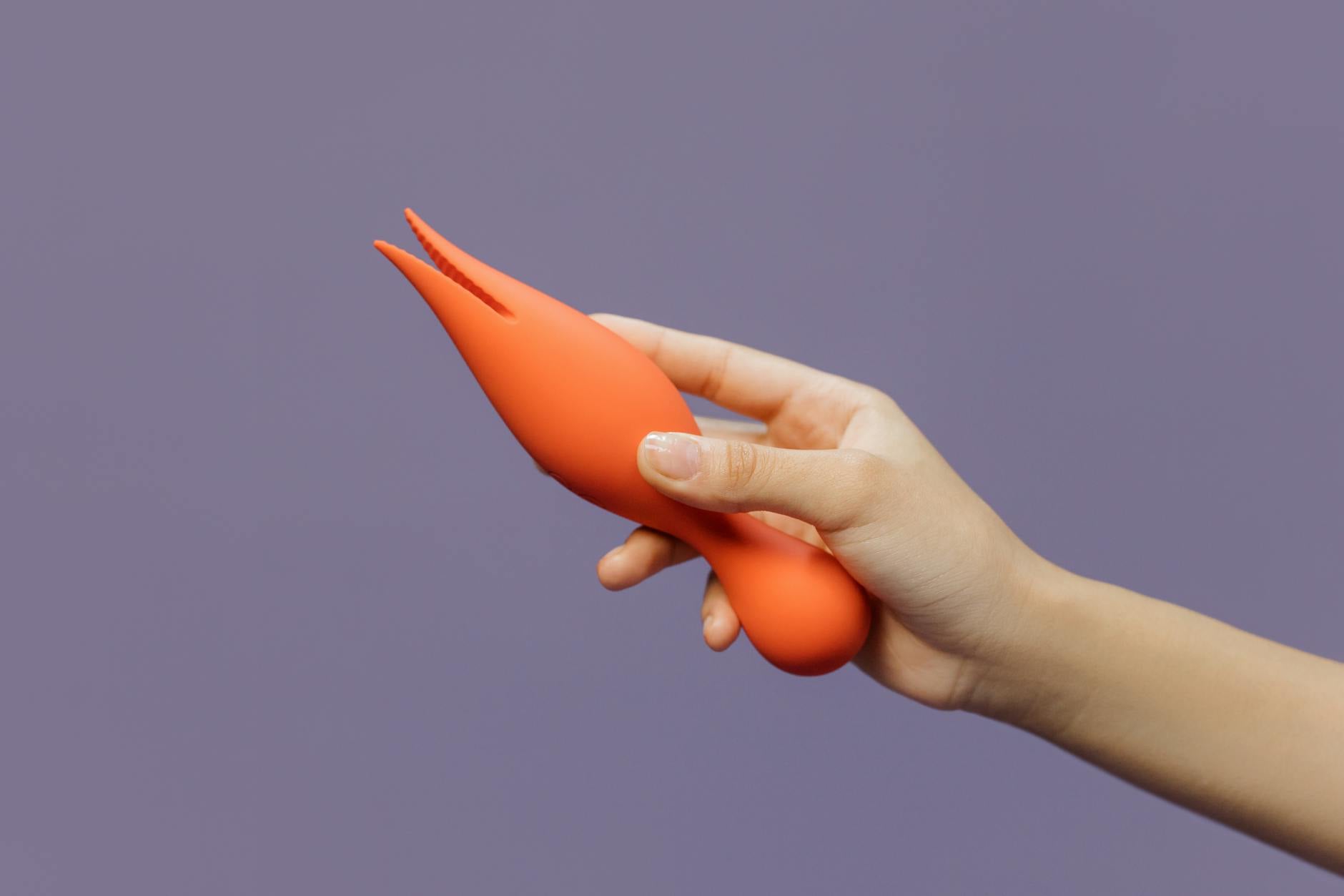 A hand holding a lemon-colored vibrator against a soft purple backdrop