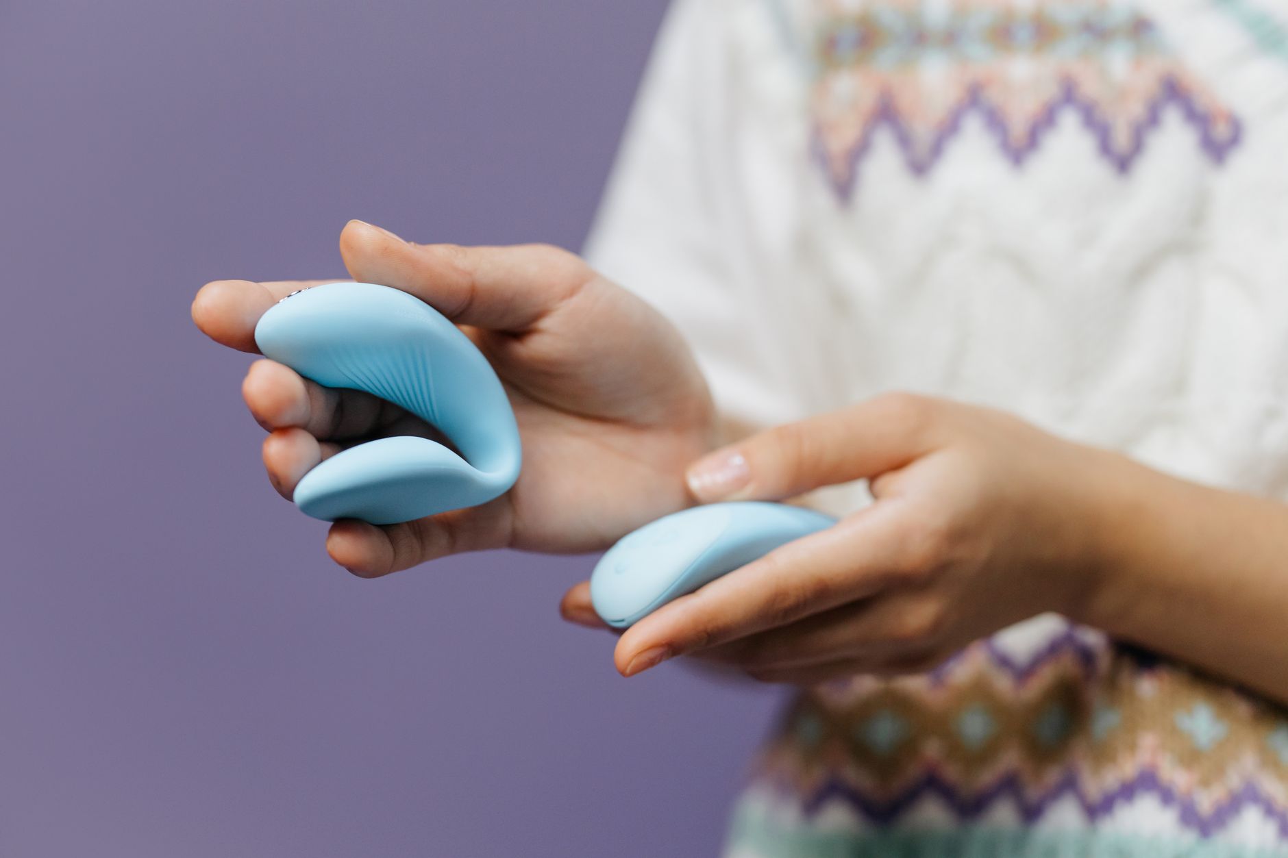 A close-up of hands holding a sleek blue vibrator against a purple background, symbolizing shared intimacy and connection.