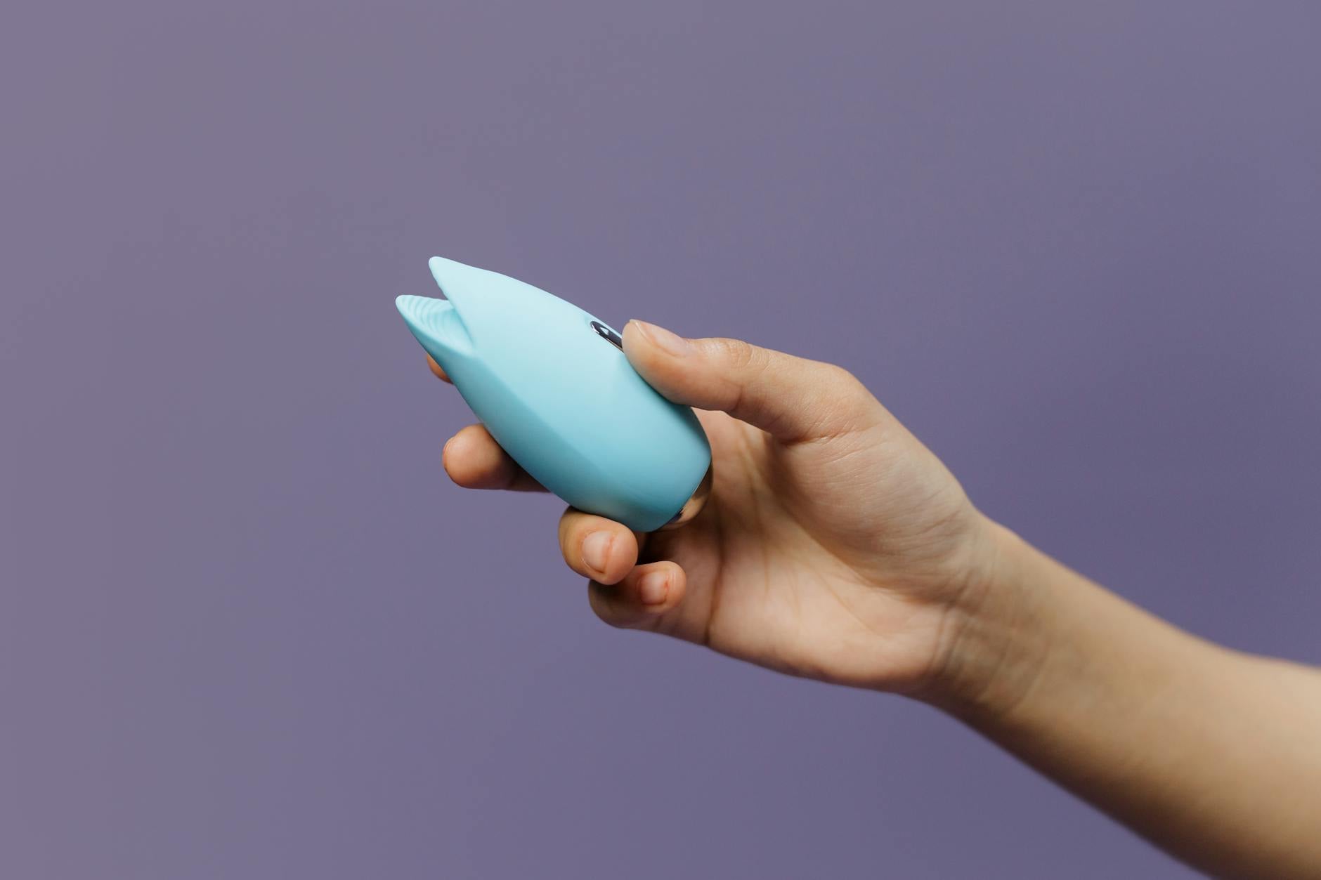 A hand holding a silicone lemon clitoral vibrator against a purple background