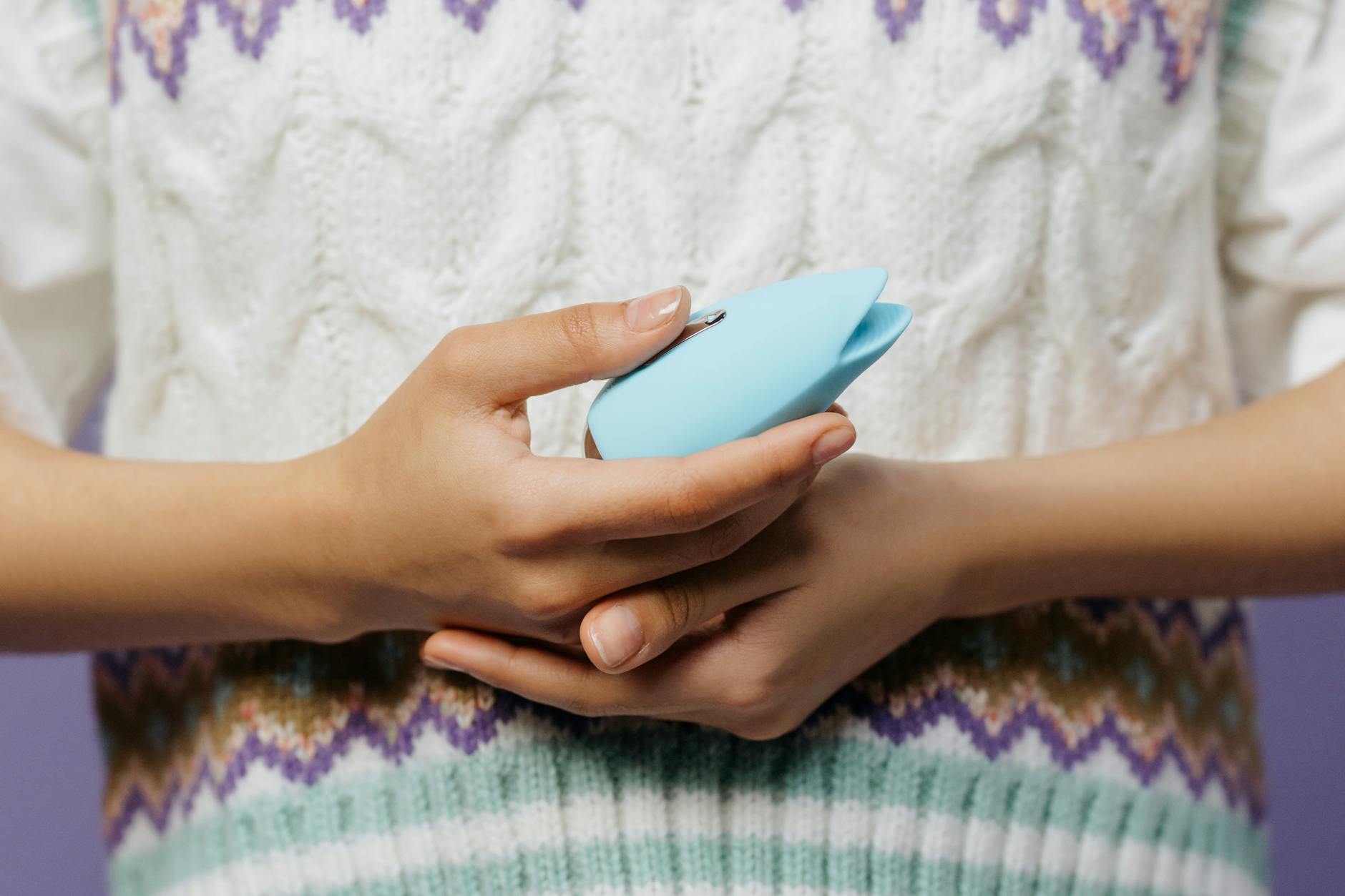 Two hands holding a blue lemon vibrator together against a knitted sweater, showing intimate connection and shared exploration.
