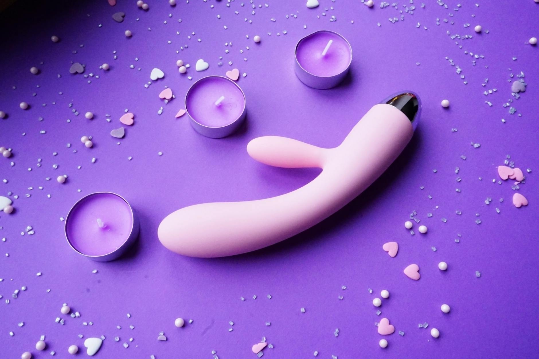 Pink lemon vibrator on purple background with candles and confetti for romantic intimacy
